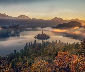 Słowenia, Jesień, Chmury, Mgła, Drzewa, Promienie słońca, Wyspa Blejski Otok, Góry Alpy Julijskie, Jezioro Bled