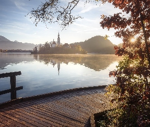 Słowenia, Promienie słońca, Wschód Słońca, Drzewa, Pomost, Góry Alpy Julijskie, Jezioro Bled, Wyspa Blejski Otok, Kościół Zwiastowania Marii Panny